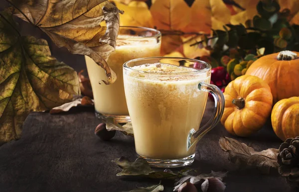 Pumpkin spiced latte or coffee in glass cup on vintage wooden table. Autumn or winter hot drink