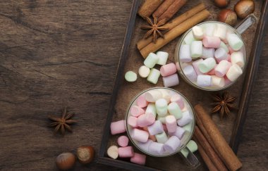 Sıcak kış ya da sonbahar içeceği kakao, beyaz çikolata, baharatlar ve renkli marşmelovlarla klasik ahşap arka planda örülmüş kalın süveter, fotokopi alanı ile üst manzara
