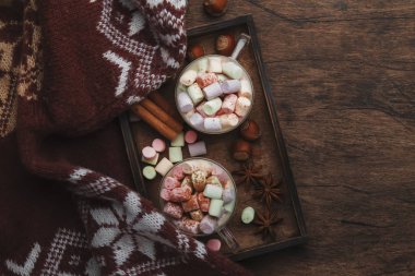Sıcak kış ya da sonbahar içeceği kakao, beyaz çikolata, baharatlar ve renkli marşmelovlarla klasik ahşap arka planda örülmüş kalın süveter, fotokopi alanı ile üst manzara