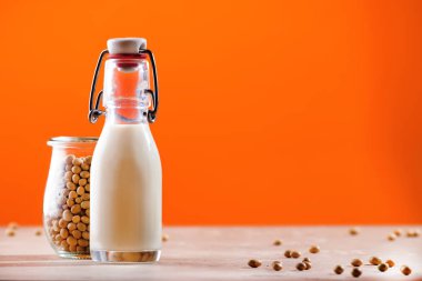 Turuncu arka planda soya sütü ve soya fasulyesi. Sütsüz süt konsepti. Vejetaryen içeceği. Boşluğu kopyala