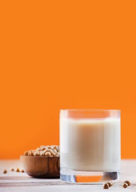 Turuncu arka planda soya sütü ve soya fasulyesi. Sütsüz süt konsepti. Vejetaryen içeceği. Boşluğu kopyala