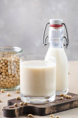 Soya sütü ve soya fasulyesi gri masada. Sütsüz süt konsepti. Vejetaryen içkisi. Boşluğu kopyala