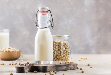Soya sütü ve soya fasulyesi gri masada. Sütsüz süt konsepti. Vejetaryen içkisi. Boşluğu kopyala