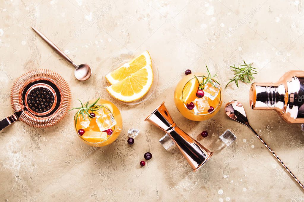 Orange Cranberry Rosemary and Vodka cocktail, copper bar tools, beige background, hard light, top view