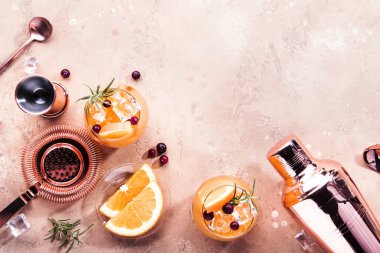Orange Cranberry Rosemary and Vodka cocktail, copper bar tools, beige background, hard light, top view