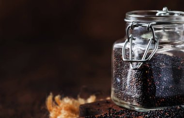 Black quinoa seeds in glass jar, vintage kitchen table background, selective focus
