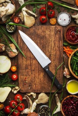 Yemek pişirme geçmişi, vejetaryen yemekleri, sebzeler, kökler, baharatlar, mantarlar ve bitkiler. Kesme tahtası, şef bıçağı. Sağlıklı gıda konsepti. Kırsal ahşap masa, üst manzara.