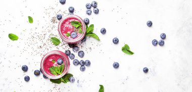 Yaban mersinli mor smoothie, chia tohumu ve nane yaprakları cam kavanozlarda beyaz arka plan, düz yatak, üst görünüm