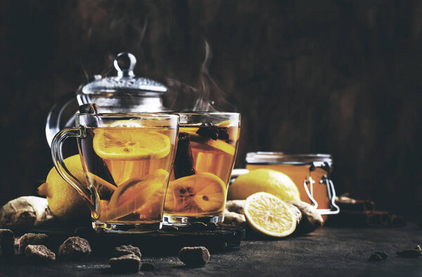 Winter or autumn hot healing tea with ginger, honey, lemon and spices in glass cup with steam, rustic wooden background