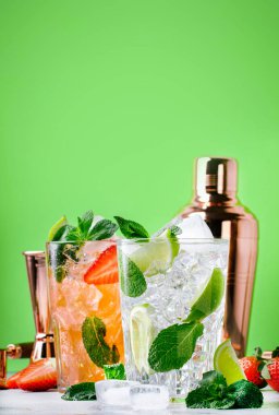 Yeşil zemin üzerinde limon, nane, çilek ve buzlu taze Mojito kokteyli. Yaz aylarında alkolsüz içecekler, içecekler ve kokteyller. Çelik bar aletleri. Boşluğu kopyala