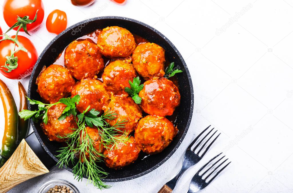 Meatballs with tomato sauce and spices in frying pan on white kitchen table background. Top View with copy space