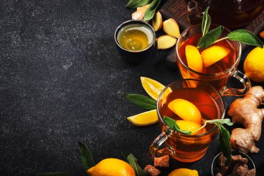 Zencefil, bal, limon ve adaçayı ile şifalı bitkisel çay. Bağışıklık güçlendirici, arka planda siyah mutfak masasında cam bardakta fotokopi alanı olan bir içecek. Üst görünüm