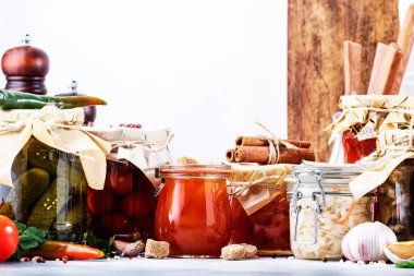 Konserve gıda konsepti. Mayalanmış, turşulu, marine edilmiş vejetaryen yemeği. Baharatlı kavanozlarda organik sebzeler ve meyveler ve beyaz mutfaktaki otlar. Ev yapımı kurnazlık.