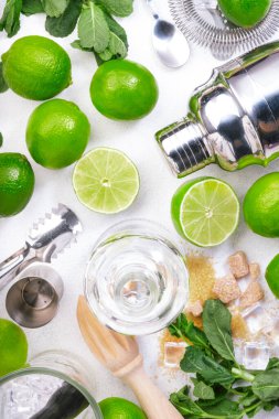 Mojito kokteyli uzun içki yapımı. Nane, kireç, buz, beyaz rom, kamış şekeri malzemeleri ve bar malzemeleri. Üst manzara, beyaz masa arkaplanı. Düz yatıyordu