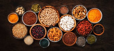 Süper yiyecekler, baklagiller, fındıklar, tohumlar ve tahıllar tahta arka planda kaselerde. Chia, spirulina, fasulye, goji üzümü, kinoa, zerdeçal, mung fasülyesi, karabuğday, mercimek, keten tohumu, yabani pirinç ve badem gibi süper yiyecekler. Boşluğu kopyala, üst görünüm