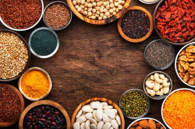Süper yiyecekler, baklagiller, fındıklar, tohumlar ve tahıllar tahta arka planda kaselerde. Chia, spirulina, fasulye, goji üzümü, kinoa, zerdeçal, mung fasülyesi, karabuğday, mercimek, keten tohumu, yabani pirinç ve badem gibi süper yiyecekler. Boşluğu kopyala, üst görünüm