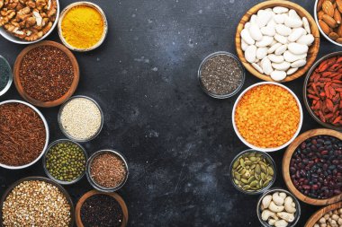 Süper yiyecekler, baklagiller, fındıklar, tohumlar ve tahıllar gri arka plandaki kaselerde seçiliyor. Chia, spirulina, fasulye, goji üzümü, kinoa, zerdeçal, mung fasülyesi, karabuğday, mercimek, keten tohumu, yabani pirinç ve badem gibi süper yiyecekler. Boşluğu kopyala, üst görünüm