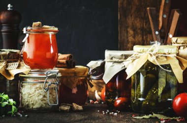 Konserve gıda konsepti. Mayalanmış, turşulu, marine edilmiş vejetaryen yemeği. Organik sebzeler ve meyveler kavanozlarda baharat ve siyah mutfak masasında bitkiler. Ev yapımı kurnazlık.