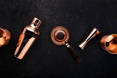 Kokteyl yapmak için bakır bar aletleri ve aksesuarları. Titretici, jigger, süzgeç, kaşık. Alkol ve içecek hazırlama konsepti. Siyah arkaplan, üst görünüm, kopyalama alanı