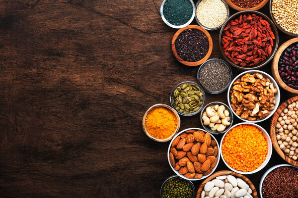 Поверхности, ножки, орехи, семена и керали, уложенные в миски на деревянном фоне. Суперфуды, такие как кия, спирулина, фасоль, ягоды годжи, киноа, куркума, фасоль, зверобой, чечевица, семена льна, дикий рис и миндаль. Копирование пространства, вид сверху
