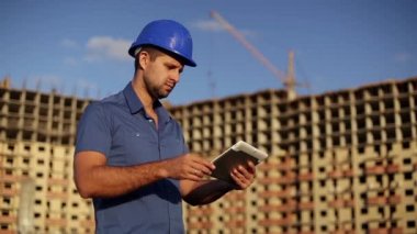 Mimar bir arka plan üzerinde bir tablet ile bir inşaat ev altında. Tablet vasıl seyir mühendisi. İnşaat, Foreman'ın çalışan bir inşaat sahasında tablet bilgisayar ile. Modern bina.  
