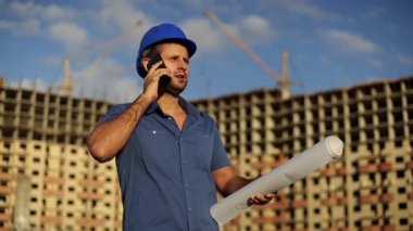 Mimar inşaat sahasında telefonda konuşuyor. Mühendis aramalar için bir arka plan üzerinde bir smartphone bir inşaat ev altında. Foreman inşaat sitesinde. Telefonda konuşurken Oluşturucu adam.