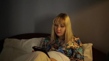 Bir cep telefonu ile yatak odasında kız. Kadın e-kitap yatak odasında okuma. Kadın geceleri okuma.