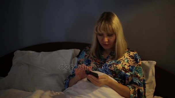 Девушка в спальне с мобильным телефоном. Женщина лежит на кровати со смартфоном. Женщина ночью в Интернете . — стоковое видео