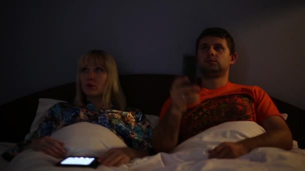 Um casal a ver televisão. Homem e mulher deitados na cama. As pessoas assistem TV à noite . — Vídeo de Stock