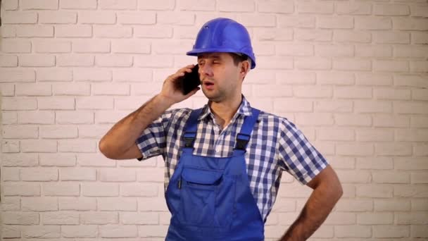 Építőmunkás beszél a telefonon. Egy építő, a munkás, a művezető, a mérnök. Egy férfi egy olyan konstrukciót sisak, a telefon. — Stock videók