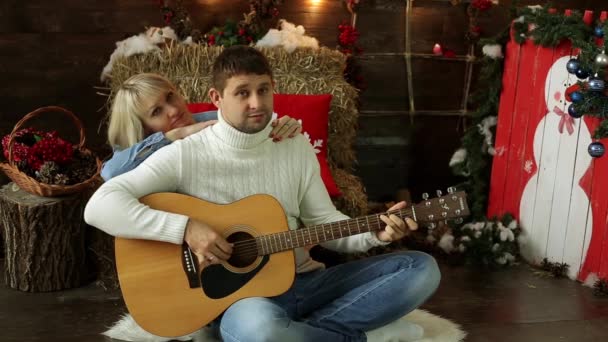 La gente toca la guitarra en un fondo navideño. Pareja joven tocando una guitarra. Hombre y mujer tocando la guitarra y cantando . — Vídeo de stock