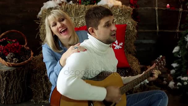 Férfi és nő gitározni és énekelni. Fiatal pár egy gitározni. Az emberek játszani a gitár a karácsonyi háttér. — Stock videók