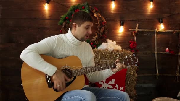 Un hombre toca la guitarra y canta. Hombre tocando la guitarra en un fondo de Navidad. El músico canta la canción de Navidad . — Vídeo de stock