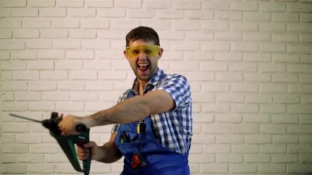 Een man in werkkleding. Werken met een boor op de bakstenen muur achtergrond. Man maakt reparaties. Een man met een perforator. Bouwvakker met hamer. — Stockvideo