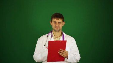Beyaz önlük erkek doktor. Doktor tıbbi geçmişini yazıyor. Doktor yeşil bir arka plan üzerine bir not defterinde yazıyor.
