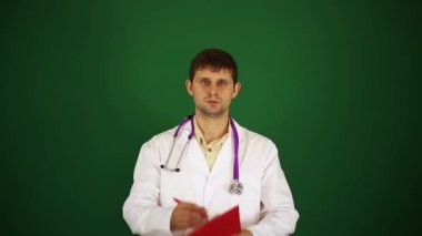 Doktor yeşil bir arka plan üzerine bir not defterinde yazıyor. Beyaz önlük erkek doktor. Doktor tıbbi geçmişini yazıyor. Doktor, Doktor, terapist resepsiyonda.
