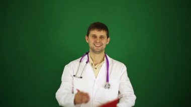 Doktor yeşil bir arka plan üzerine bir not defterinde yazıyor. Beyaz önlük erkek doktor. Doktor tıbbi geçmişini yazıyor. 