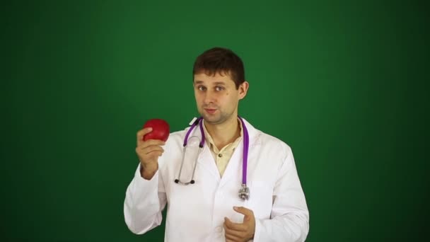 Мужчина врач на заленовом фоне. Доктор держит красное яблоко . — стоковое видео