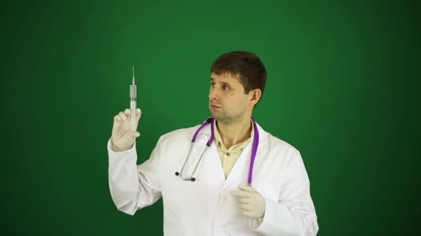 Junger Arzt mit Spritze auf grünem Hintergrund. Behandlung, Spritze und Arzt im weißen Laborkittel. Arzt rät von Spritzen ab. Arzt hat Angst vor Spritzen. — Stockvideo