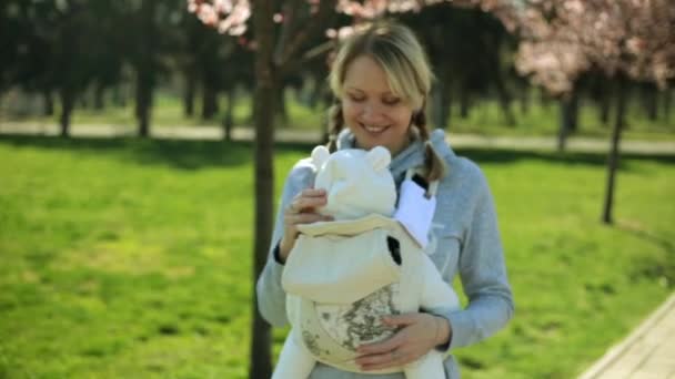 Donna con bambino in natura. Una giovane madre con un bambino in fionda. Mamma cammina con il bambino nel parco. Un bambino piccolo in una fionda . — Video Stock