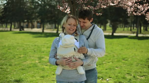 Young beautiful family with baby. Mom, dad and baby in the park. European family with a child in a sling. Young family with child in park. — Stock Video