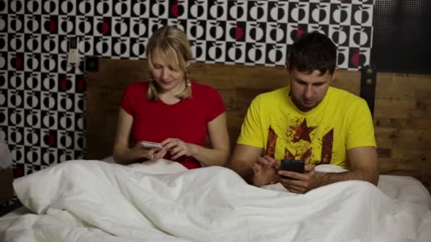 Uomo e donna a letto con gli smartphone. Coppia giovane di sera su un letto su Internet con smartphone . — Video Stock