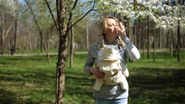 Hermosa mujer está caminando en el parque con el bebé. Mamá lleva al bebé en un cabestrillo . — Vídeos de Stock