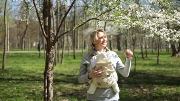 En kvinna med ett barn nära ett blommande träd. Mamma med bebis i parken. — Stockvideo