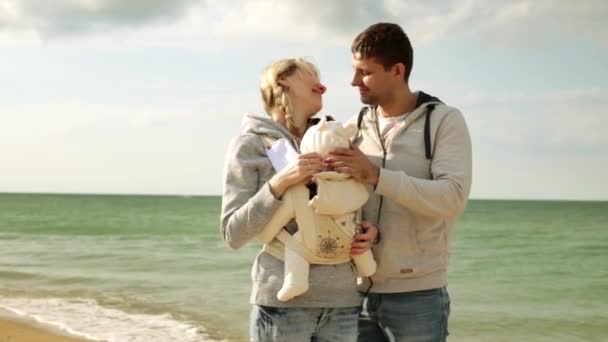 Familie mit Kind am Strand. junge Eltern mit einem Baby im Tragetuch. junge Familie mit Kind auf dem Hintergrund des Meeres. — Stockvideo
