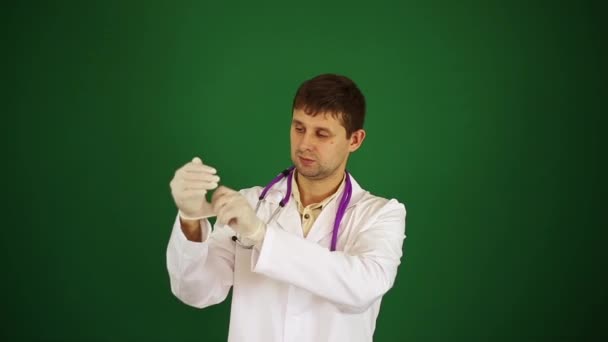 Läkaren sätter på medicinska handskar. En manlig läkare på en grön bakgrund. — Stockvideo
