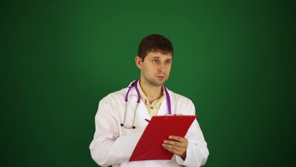 Doctor on a green background. Doctor writes on the tablet. A male doctor writes in a notebook. — Stock Video