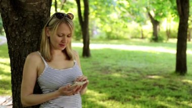 Kadın parkta bir smartphone. Kız, bir smartphone için Internet'i kullanır. Bir adam ile doğanın içinde smartphone.