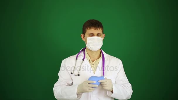 A doctor in a medical mask holds an enema. Doctor with enema on a green background. — Stock Video