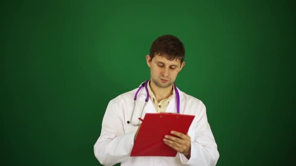 El doctor sobre un fondo verde escribe en un bloc de notas. El doctor escribe la historia clínica . — Vídeo de stock